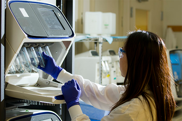 Cancer scientist loading tubes into a lab machine. Photo by the National Cancer Institute.